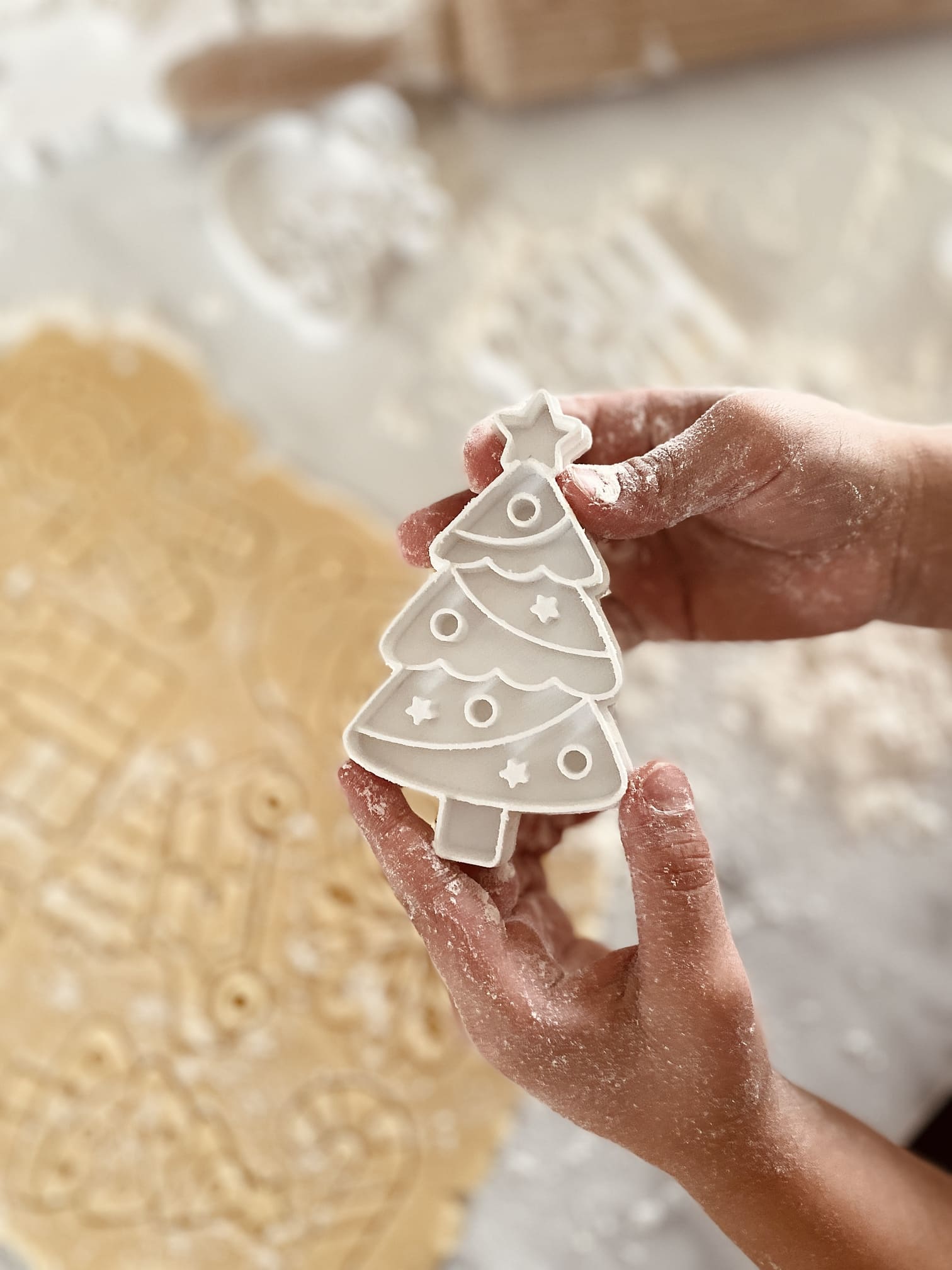 Emporte-pi&egrave;ce sapin de No&euml;l en main au-dessus d'une p&acirc;te &agrave; bredele farin&eacute;e